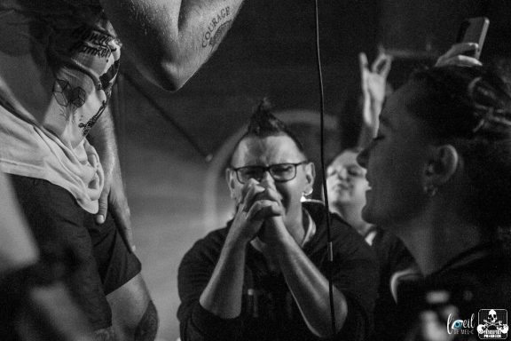 People at a concert, focused on the performer, with a mix of expressions and excitement.