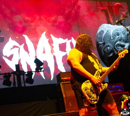 Musician playing guitar on stage with bold visuals in the background.