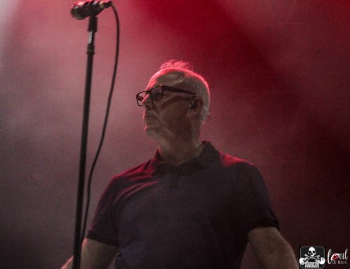 A singer on stage with a microphone, illuminated by red and purple lights.