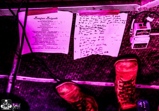 Red boots beside setlists and pedals on a textured surface with purple lighting.