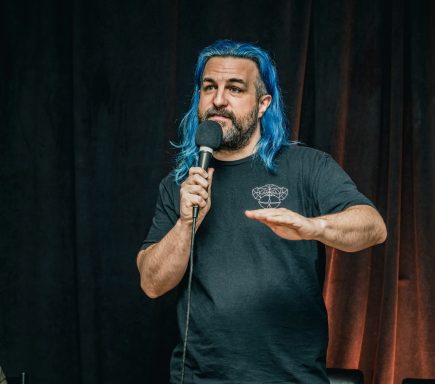 Rouge Pompier - Radiothon CKRL 89,1 Man with blue hair holds a microphone and gestures while speaking on stage.