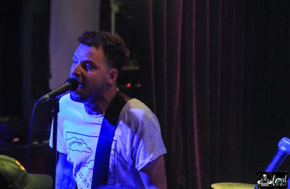 Musician performing on stage, singing into a microphone with dramatic lighting.