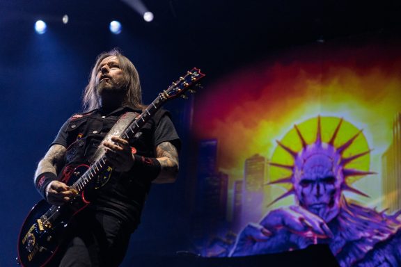 Musician playing guitar onstage with a vibrant, artistic background.