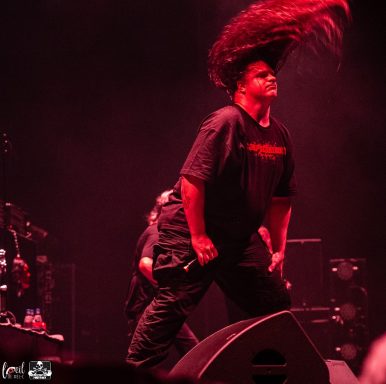 A performer with long hair swings it passionately during a live concert.