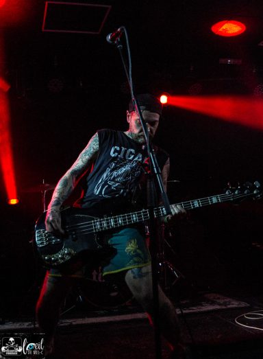 Straightline - L'Anti-Bar & Spectacles A musician plays bass on stage with dramatic lighting and an energetic pose.