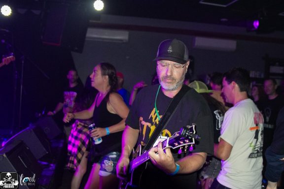 A guitarist performing on stage with an audience enjoying the music.