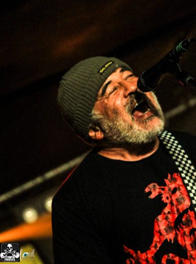 Man in a beanie singing passionately into a microphone on stage.