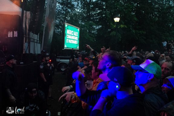 Crowd enjoying a concert under dim lighting, with a green illuminated sign in the background.