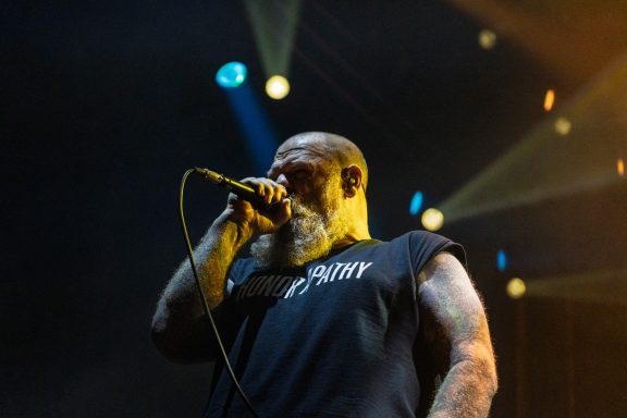 Musician passionately performing on stage with a microphone, vibrant lights in the background.