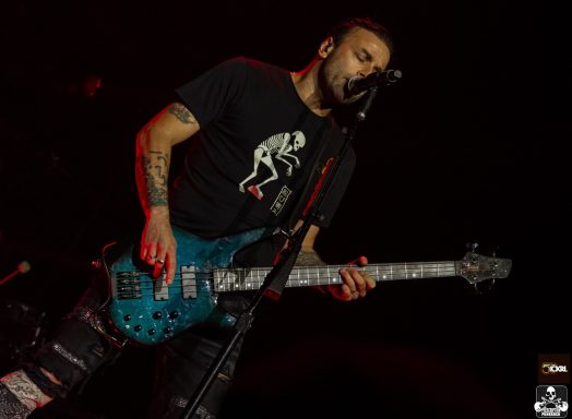 Male musician playing a blue bass guitar and singing on stage.