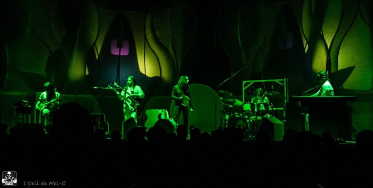 A band performs on stage with green lighting and abstract background.
