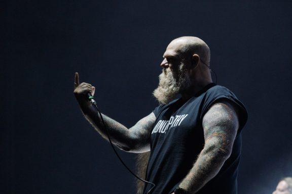 A man with a beard and tattoos raises his middle finger during a performance.