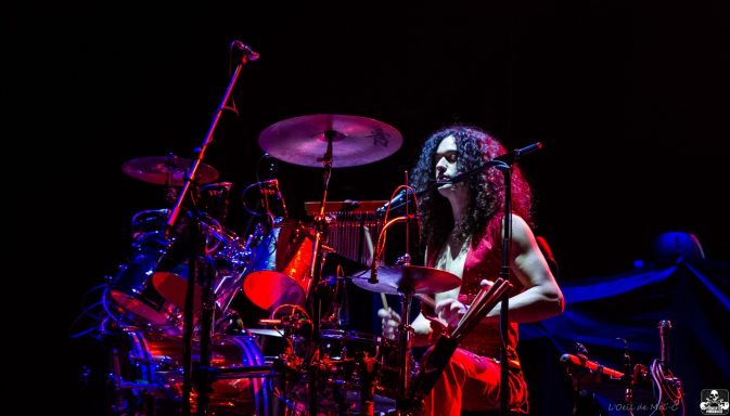 Female drummer in a vibrant red outfit performing on stage.