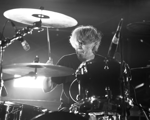A drummer performing passionately on stage with dynamic lighting.