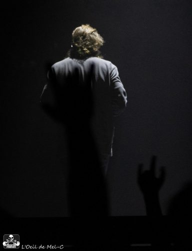 Silhouette of a performer with audience hand raised in rock gesture against a dark background.