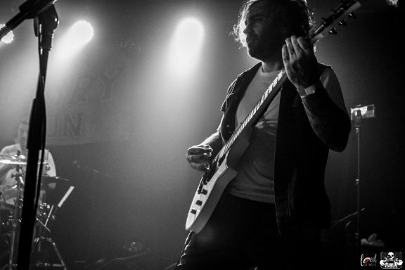 Musician playing guitar on stage with dramatic lighting in a live performance.