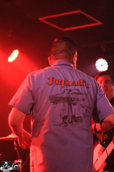 Person in a blue shirt with "Jaguar" logo, performing on stage with red lighting.