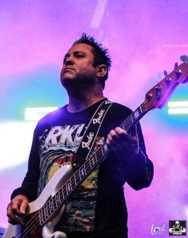 Musician playing bass guitar on stage with colorful lighting in the background.