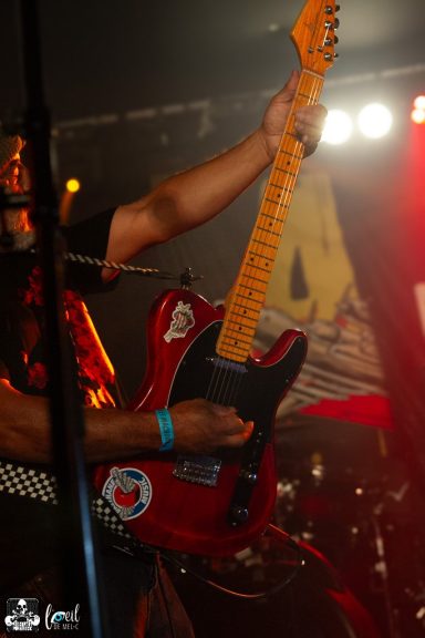 Person playing a red electric guitar on stage with bright lights in the background.