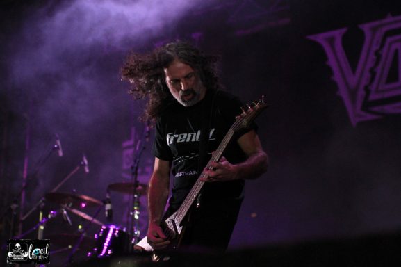 Musician playing electric guitar on stage with dramatic lighting and energetic motion.