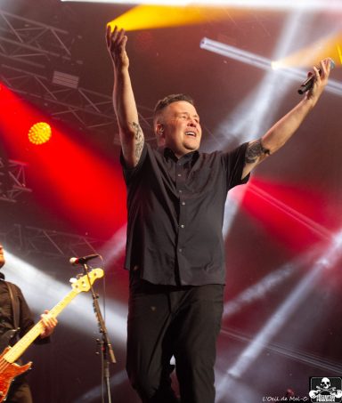 A performer on stage with raised arms, surrounded by dynamic lighting and band members.