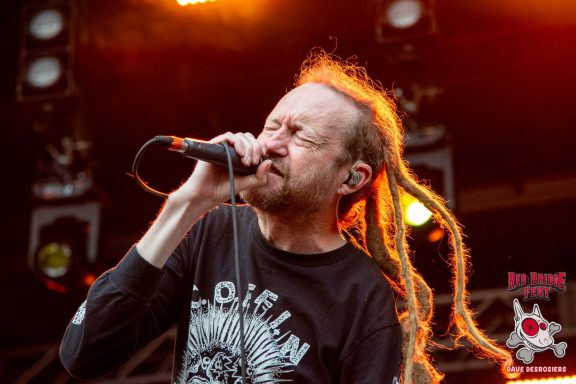 Singer with long dreadlocks performing on stage, microphone in hand, intense expression.