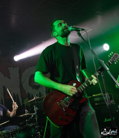 Musician with a guitar performs on stage, green lights illuminating the scene.