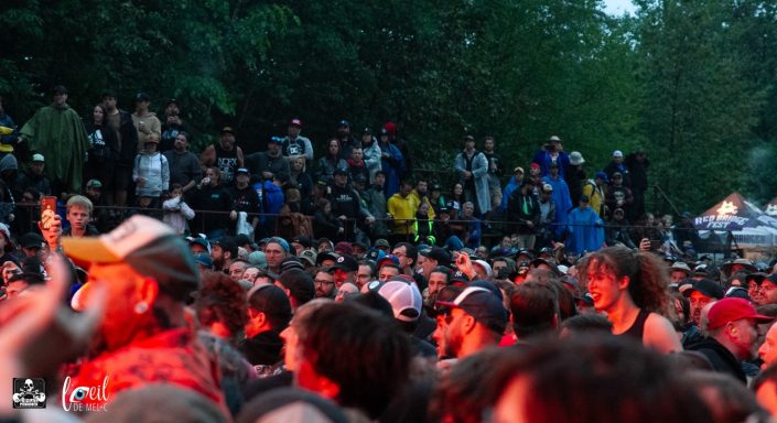 Crowd of people at an outdoor event, with green trees and a lively atmosphere.