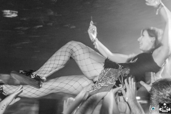 A performer crowd-surfing while fans support her, in a dynamic black-and-white setting.