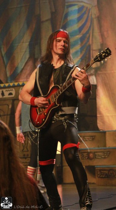 Musician playing an electric guitar, wearing a red bandana and black outfit on stage.