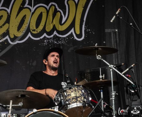 Drummer performing passionately on stage with a dark backdrop.