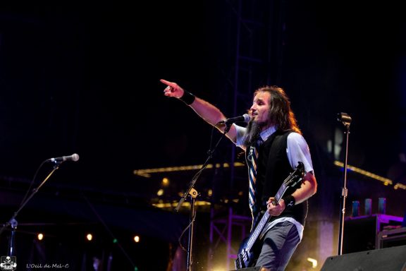 Musician performing energetically with a guitar and pointing to the audience.