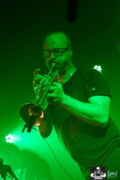 Musician playing trumpet on stage with green lighting.