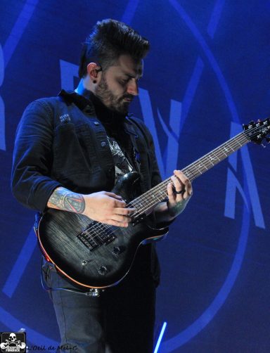 Musician playing electric guitar on stage with dramatic blue lighting.