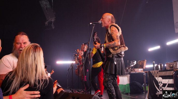 A live band performing on stage with energetic fans in the foreground.
