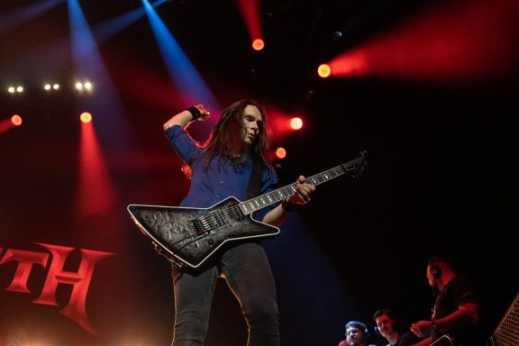 Musician playing an electric guitar on stage with colorful stage lights.