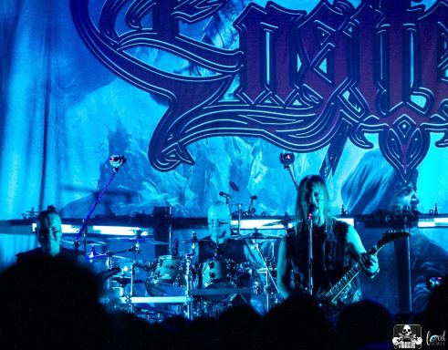 Musicians performing on stage with blue lighting and a large backdrop.