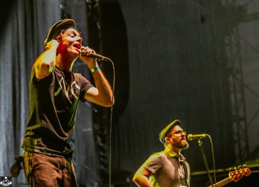 Two musicians performing on stage, with one singing and the other playing guitar.