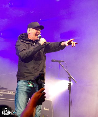 A performer sings into a microphone on stage, pointing during a lively musical performance.