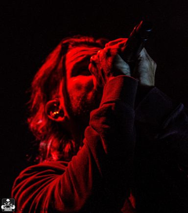 A singer passionately performing on stage with red lighting.