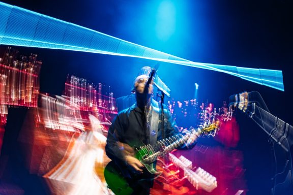 +LIVE+ - Centre Videotron Musician performing on stage with a guitar and colorful light effects in the background.