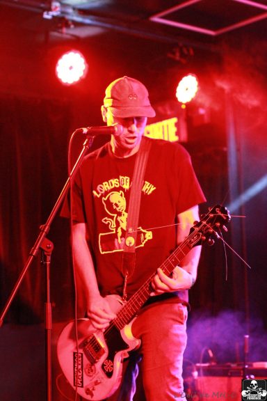 Musician playing guitar on stage with red lighting and microphone.