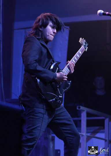 Person playing an electric guitar on stage with dramatic lighting.