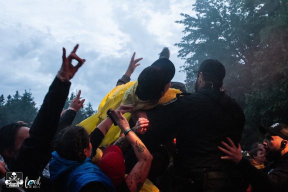 Crowd cheering at an outdoor event, with people lifting a performer in a yellow outfit.