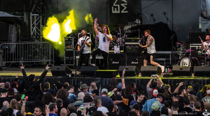 A band performs energetically on stage with an enthusiastic crowd in front.