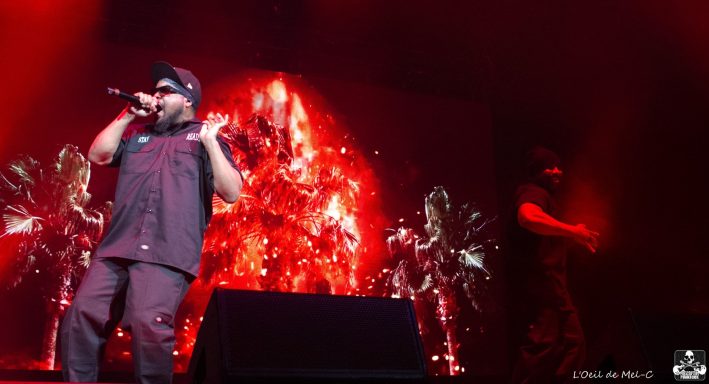 Performer singing on stage with a vibrant red background and dramatic lighting effects.
