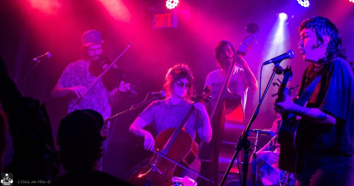 Musicians performing on stage with various instruments in a vibrant, colorful lighting.