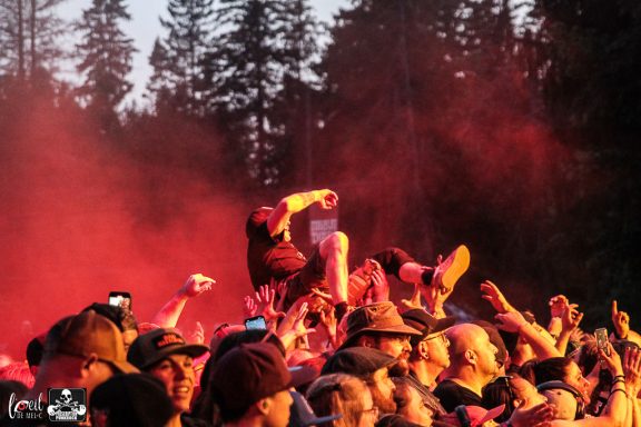 A crowd at a concert with red lighting, cheering and enjoying the performance.