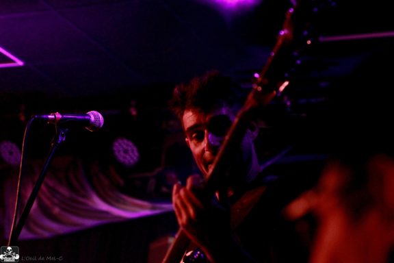 Musician playing guitar on stage with vibrant purple lighting.