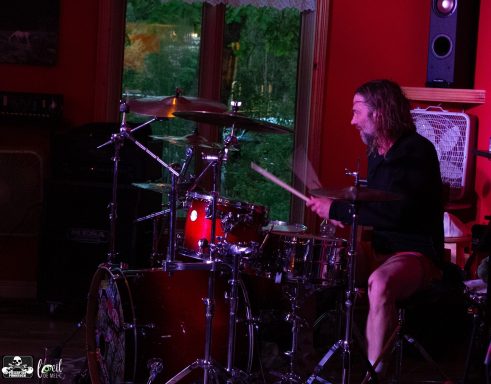 Drummer performing in a lively music venue with vibrant red walls.